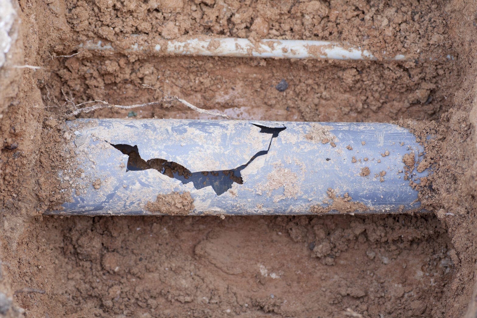 A blue-gray sewer line is cracked and surrounded by dirt and requires emergency septic service