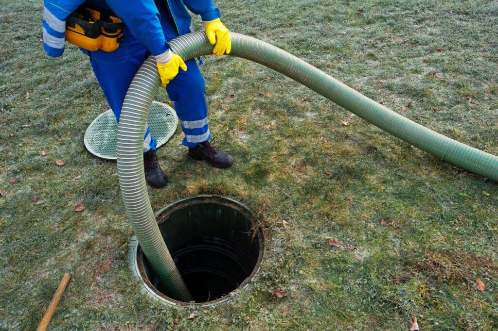 A service technician snakes a hose down a septic drain to pump it out.