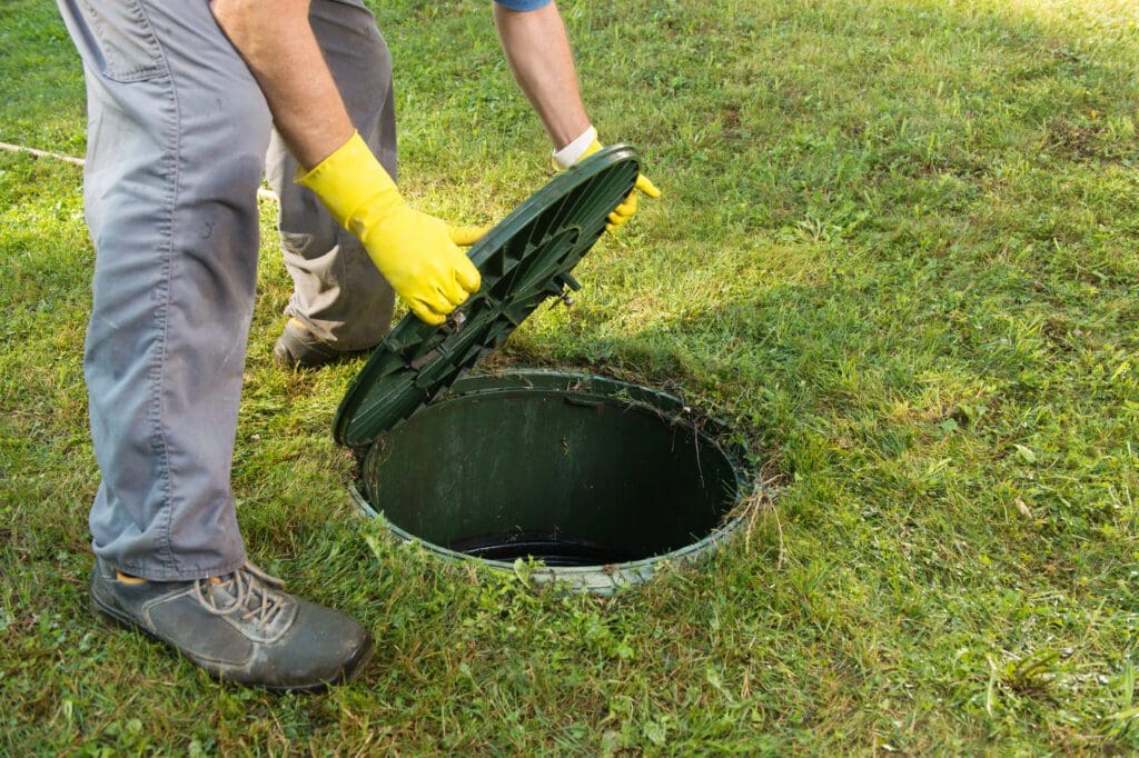 A man removes the lid from a septic tank to inspect it.