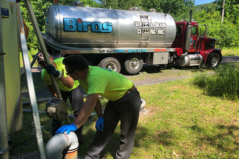 Two workers from Biros Septic & Drain Cleaning work with a septic truck in the background.